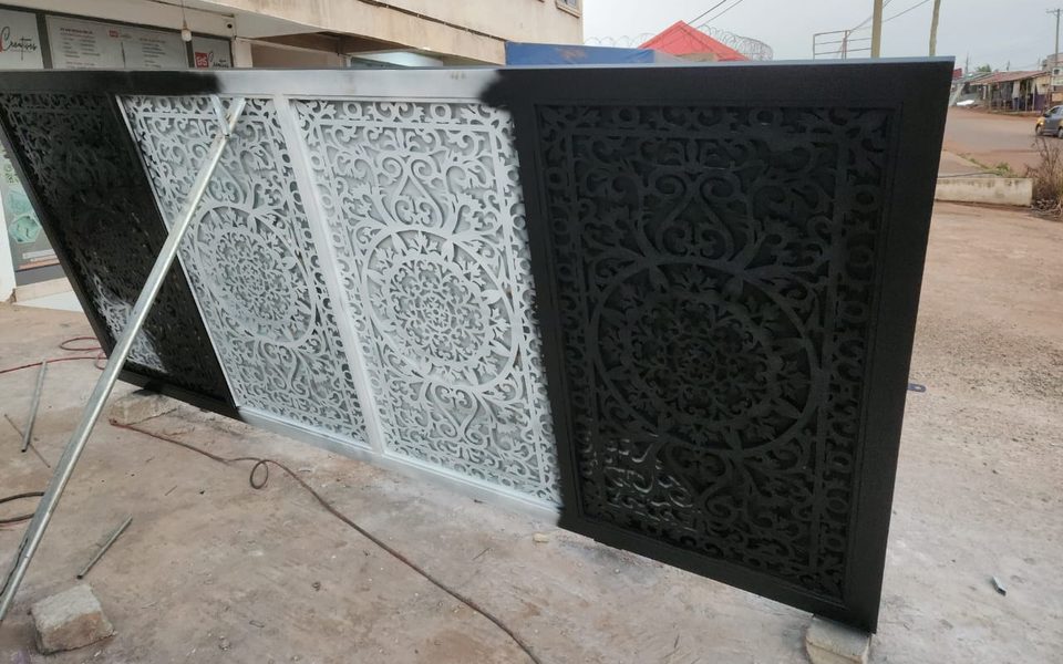 Ornate laser-cut gate panels being painted black