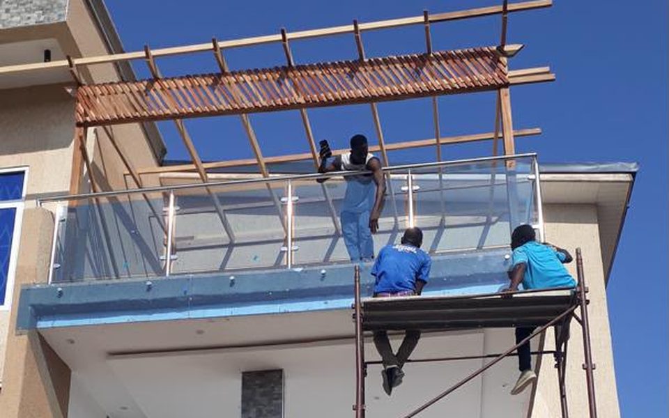 Workers installing a glass balcony balustrade under a timber pergola